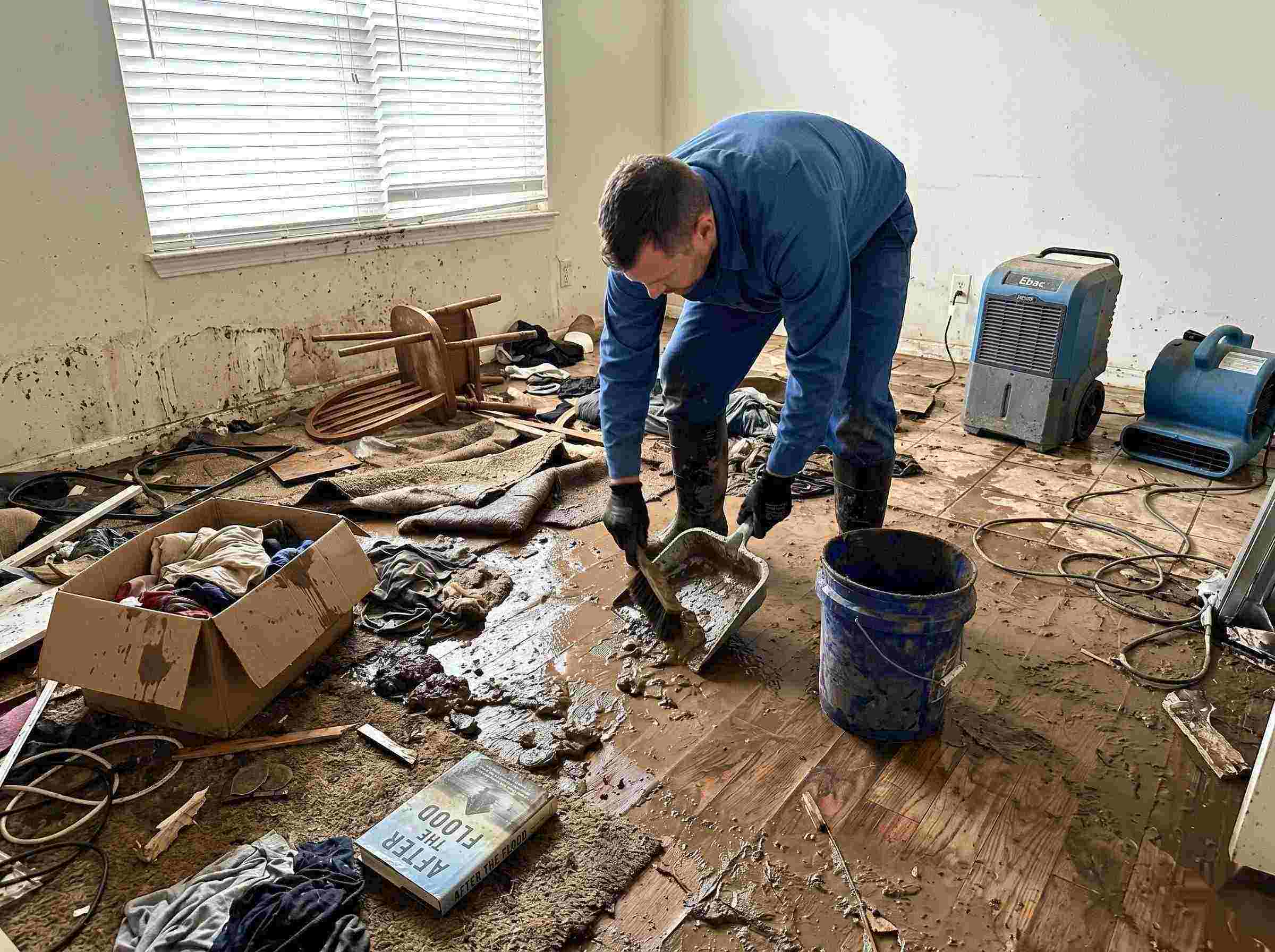 Realistic photo of a technician performing mud and debris removal after a home flood in Reno, showing soaked furniture, wet flooring, and scattered debris during post-flood cleanup.